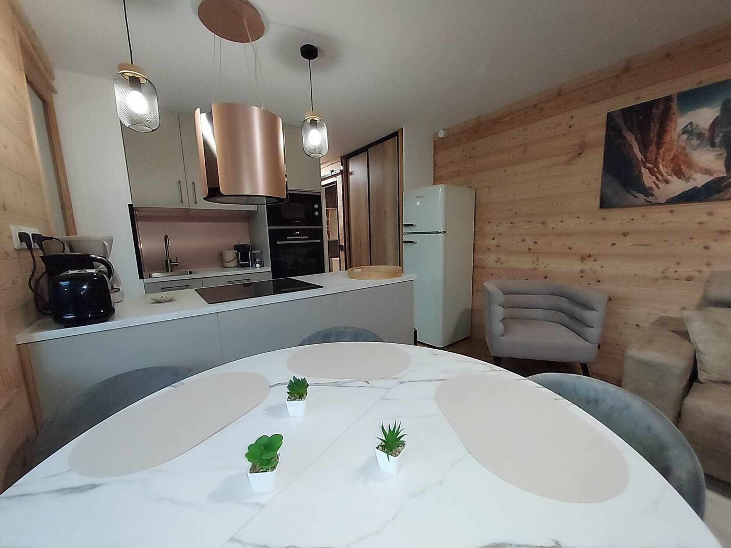 A modern kitchen with a central island, a dining table with chairs, and a painting on the wall.