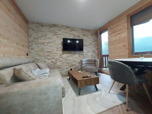 Ein modernes Wohnzimmer mit Steinwand, Flachbildfernseher, Sofa, Couchtisch und einem Essbereich mit einem Stuhl.