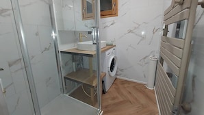 Ein kleines Badezimmer mit Duschkabine aus Glas, integriertem Waschbecken, einem kleinen Fenster und einer Waschmaschine.