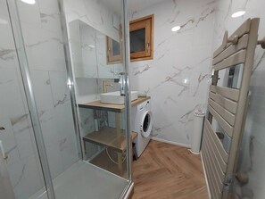 Ein kleines Badezimmer mit Duschkabine aus Glas, integriertem Waschbecken, einem kleinen Fenster und einer Waschmaschine.
