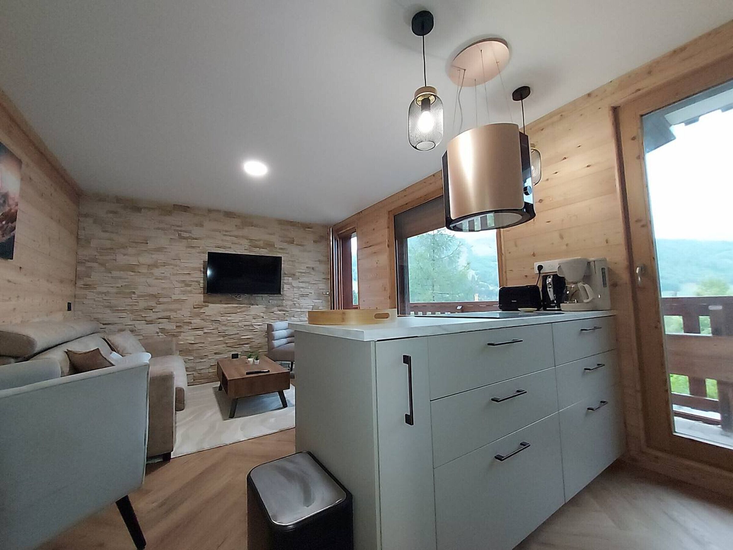 A modern kitchen with a stone wall, a flat-screen TV, and a coffee maker.
