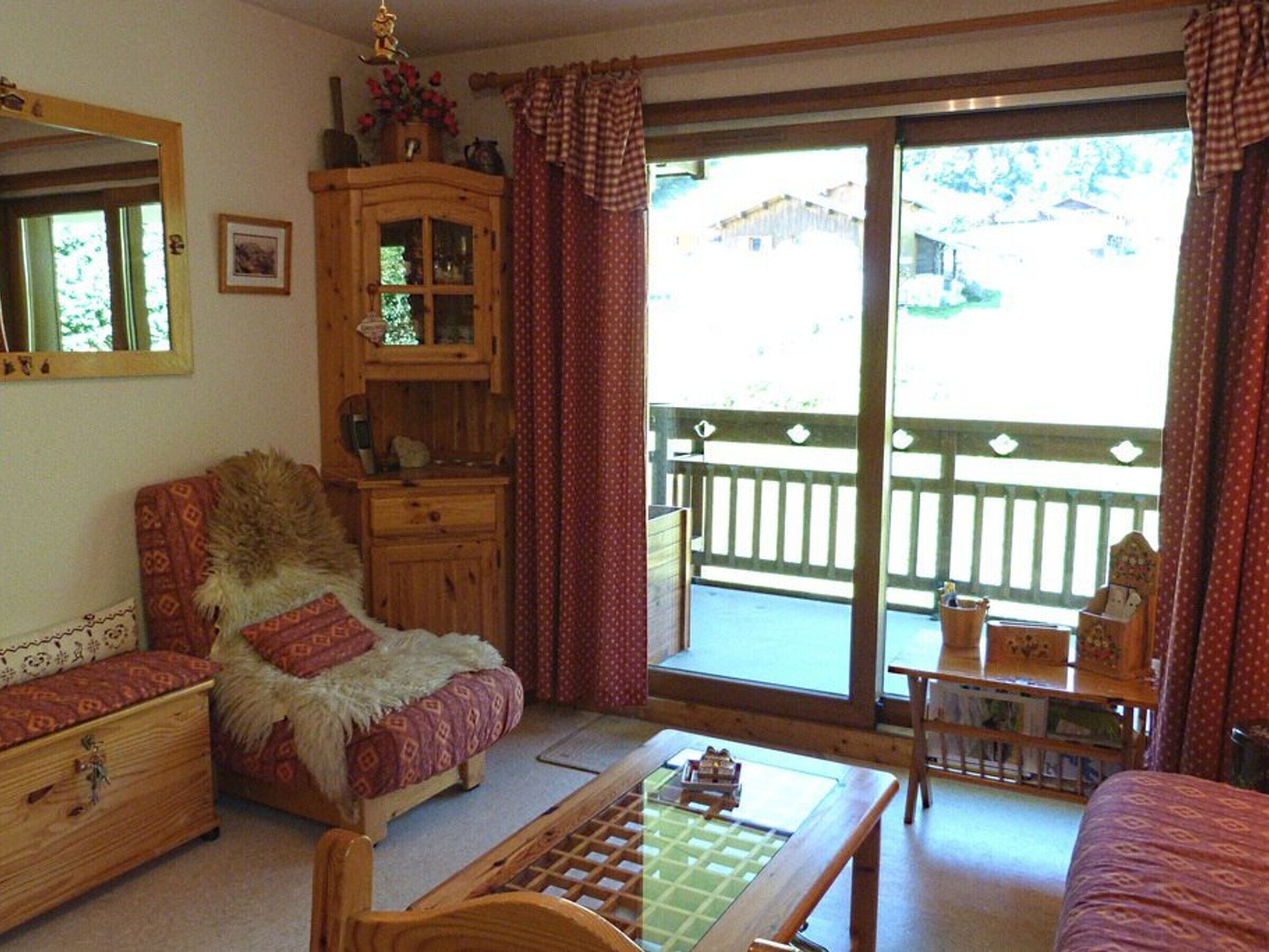 A cozy room with a wooden cabinet, a cushioned chair, a small table, and a view of the outdoors through a sliding door.