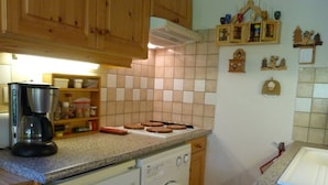 Eine Küche mit Holzausstattung, einer Kaffeemaschine, einer Waschmaschine und einer gefliesten Spritzschutzwand.