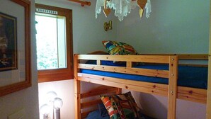 Ein Stockbett mit blauer Matratze, ein kleiner Nachttisch mit Lampe und ein Fenster mit Blick auf Grünflächen.