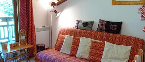 Una habitación acogedora con un sofá estampado, una mesita con un tablero de ajedrez y una estructura de madera montada en la pared.