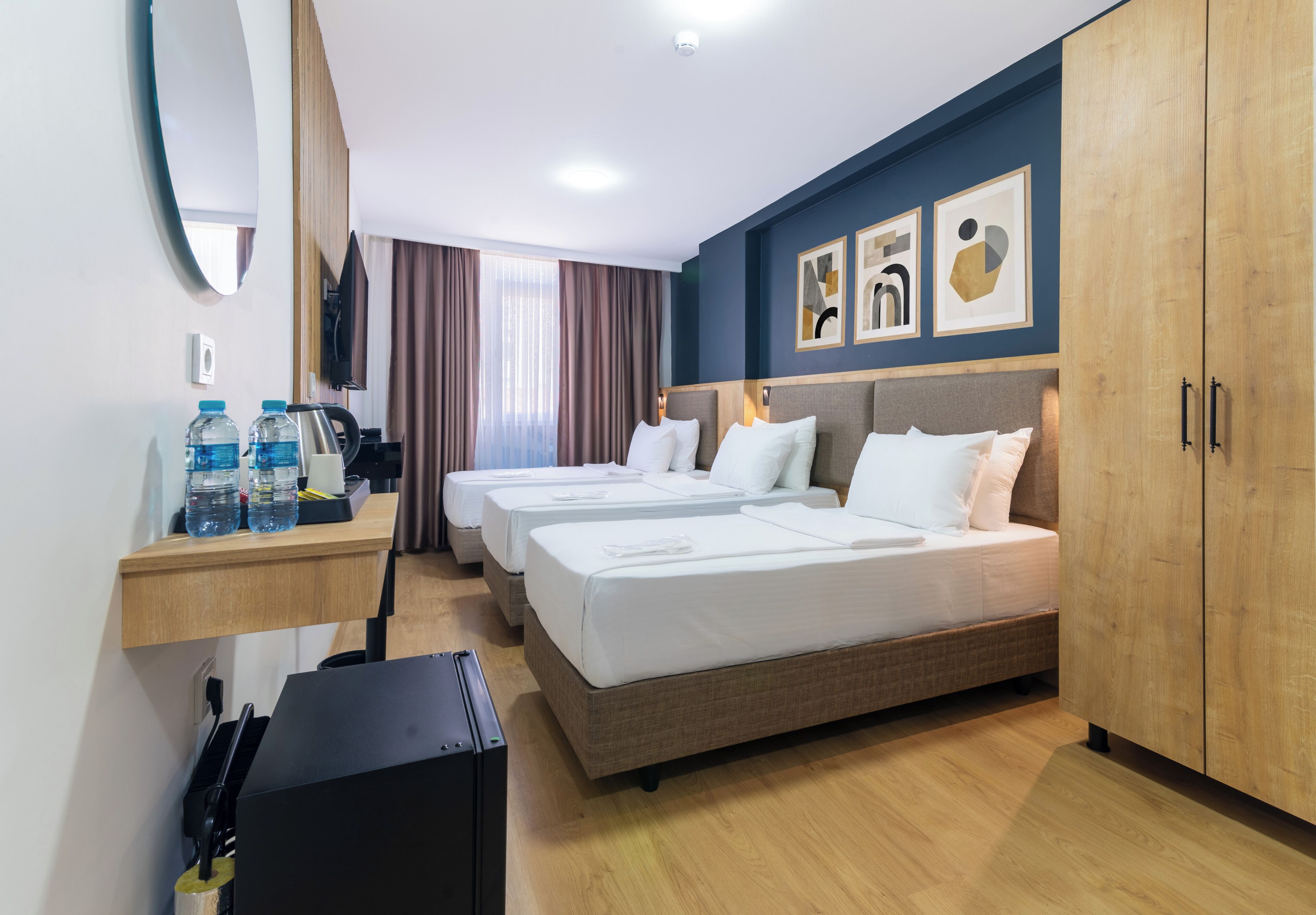 Quarto de hotel com duas camas, uma secretária com garrafas de água, uma televisão e obras de arte na parede.