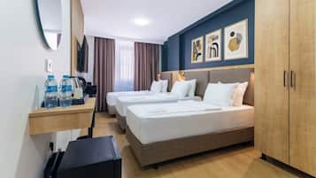 Quarto de hotel com duas camas, uma secretária com garrafas de água, uma televisão e obras de arte na parede.
