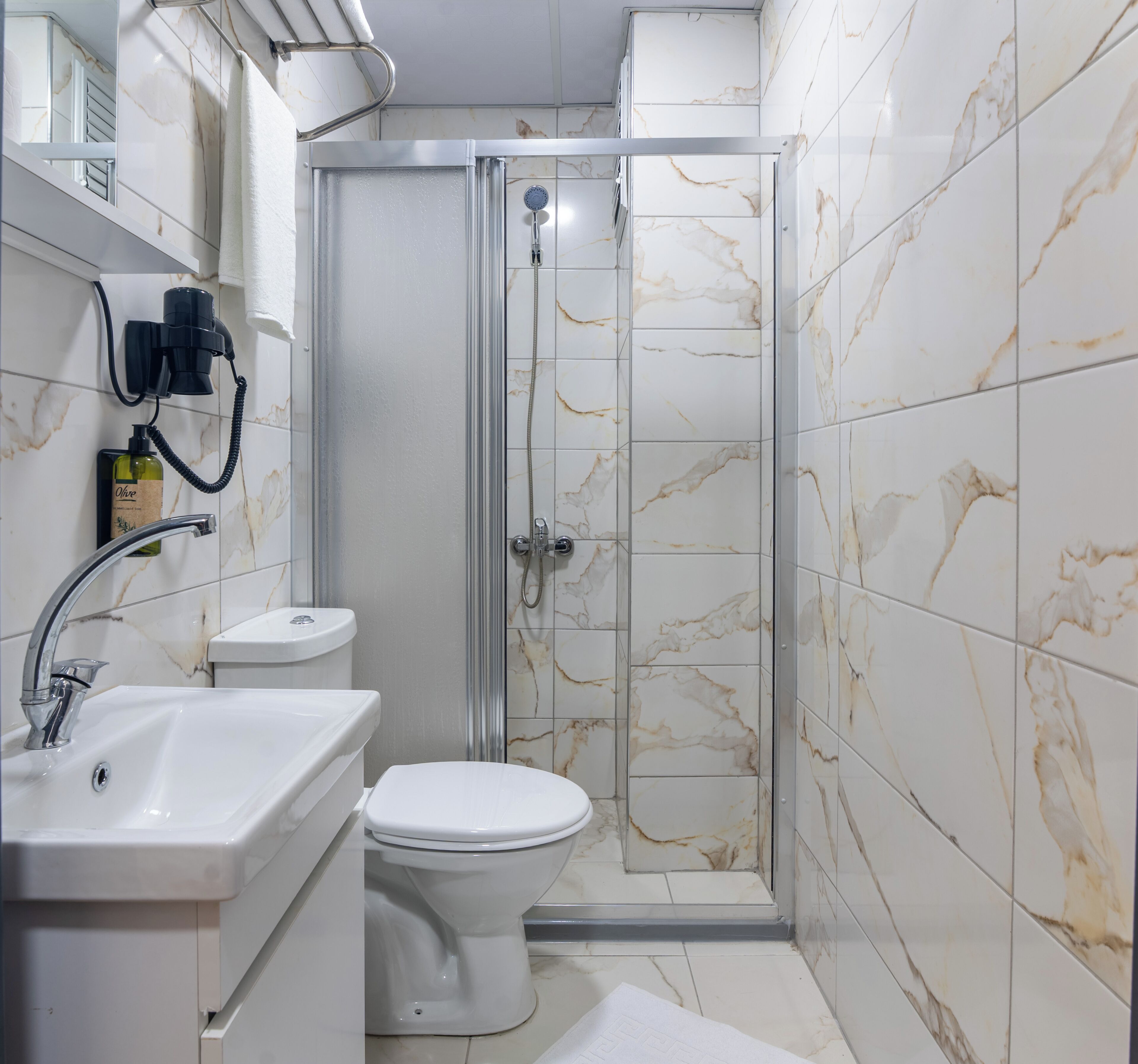 A bathroom with a shower, toilet, sink, and a bottle of olive oil.