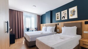Una habitació d'hotel amb dos llits, un sòl de fusta, una finestra amb cortines i una obra d'art a la paret.