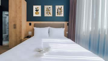 Quarto de hotel com uma cama grande, um guarda-roupa de madeira, uma mesa de cabeceira com telefone e arte abstrata na parede.