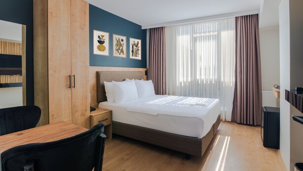 Habitació d'hotel amb llit, escriptori, cadira, armari i obra d'art a la paret.