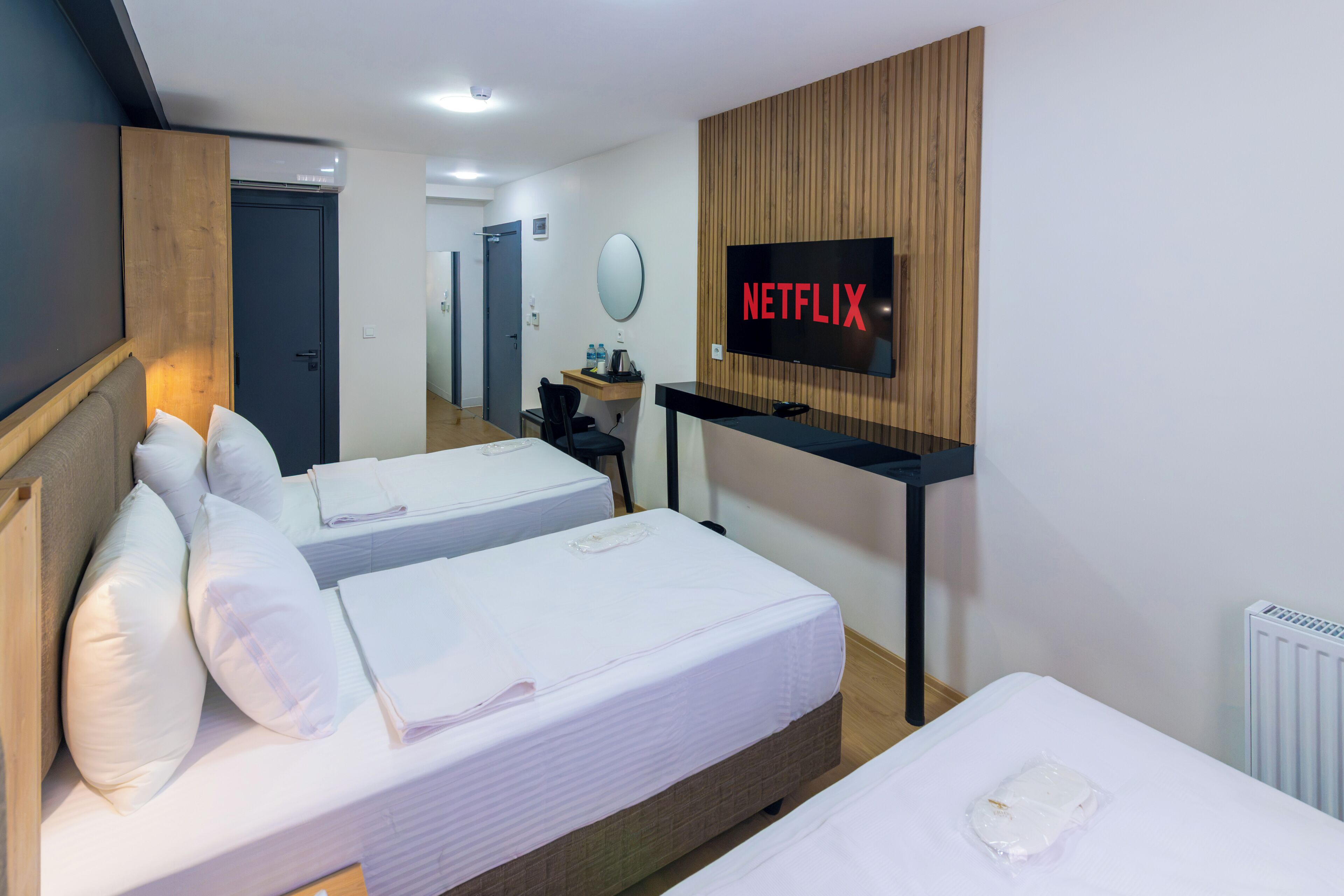 Ein Hotelzimmer mit zwei Betten, einem an einer Holzvertäfelung angebrachten Fernseher und einer Tür zu einem Flur.