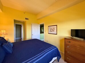 Ein Schlafzimmer mit einem Bett, einem Schminktisch, einem Fernseher und einer Tür zu einem anderen Raum.