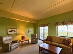A living room with a sofa, armchairs, a coffee table, and a lamp. There are two windows with curtains, and a picture frame on the wall. - 2nd floor condo overlooking Grandfather mountain- hot tub- views (Sugar Mountain)