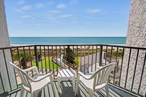 A balcony with two white plastic chairs, a small table, and a view of the beach and ocean. - Oceanfront Two Queen Room + Beach + Dog Friendly (Myrtle Beach)