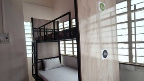 Une chambre avec des lits superposés, un ventilateur de plafond, une fenêtre avec des barreaux et une pancarte indiquant le numéro de chambre : A5.
