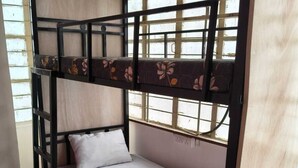 Un lit superposé avec un matelas et des oreillers, une fenêtre donnant sur un paysage agréable et une porte en bois.