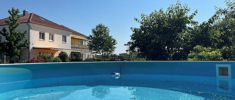 A swimming pool with a clear blue water surface, surrounded by greenery and a building with a tiled roof.