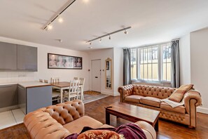A modern living room with a brown leather sofa, a dining area with white chairs, and a kitchen with grey cabinets. - Host Stay - 37 Regency Square (Brighton)