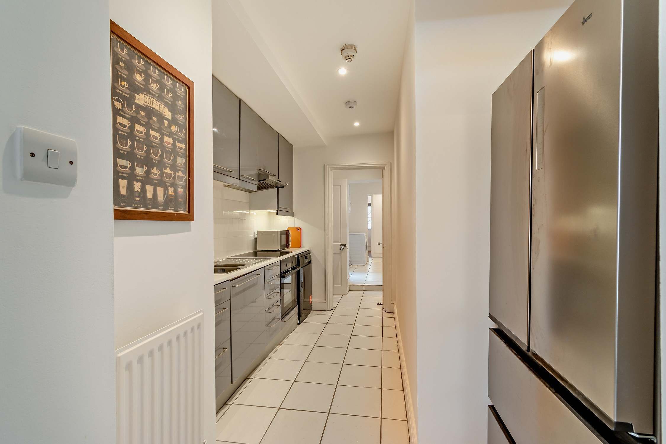 A modern kitchen with stainless steel appliances, a tiled backsplash, and a framed coffee chart on the wall.
