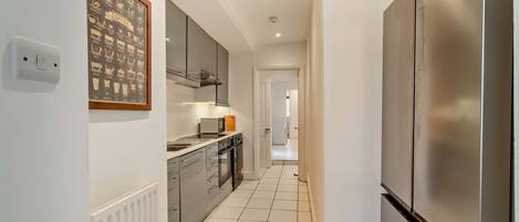 A modern kitchen with stainless steel appliances, a tiled backsplash, and a framed coffee chart on the wall.