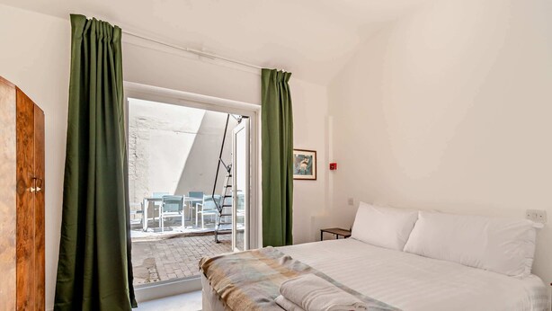 Een slaapkamer met een bed, een raam met gordijnen, een houten vloer en een schilderij aan de muur.