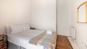 Een slaapkamer met een bed, nachtkastje, radiator en een spiegel aan de muur.
