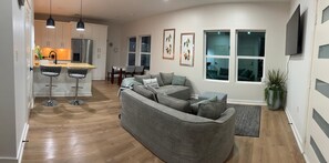 A modern living room with a grey sectional sofa, a dining area with a table and chairs, and a kitchen with white cabinets and a stainless steel refrigerator. - Charming 3-bedroom rooms with 2 full bath  house with AC in Houston area!  (Houston)