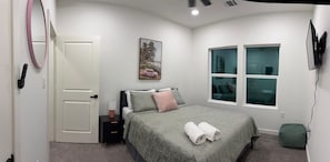 A bedroom with a bed, a nightstand, a wall-mounted TV, a window with a view, and a door. - Charming 3-bedroom rooms with 2 full bath house with AC in Houston area! (Houston)