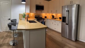 Uma cozinha moderna com ilha central, eletrodomésticos de aço inoxidável e uma TV de tela plana instalada acima do fogão.