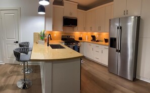 A modern kitchen with a central island, stainless steel appliances, and a flat-screen TV mounted above the stove. - Charming 3-bedroom rooms with 2 full bath  house with AC in Houston area!  (Houston)
