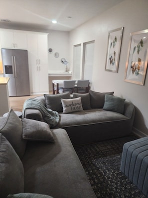 A modern living room with a grey sofa set, a patterned rug, and a kitchen in the background. - Charming 3-bedroom rooms with 2 full bath house with AC in Houston area! (Houston)