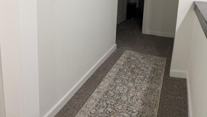 Um corredor com um tapete estampado, uma obra de arte emoldurada na parede e uma porta que dá para outro quarto.