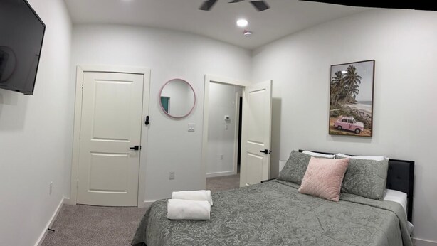 Quarto com cama, televisão fixada na parede, uma porta e um quadro emoldurado.