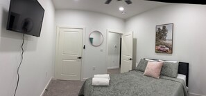 A bedroom with a bed, a television mounted on the wall, a door, and a framed picture.