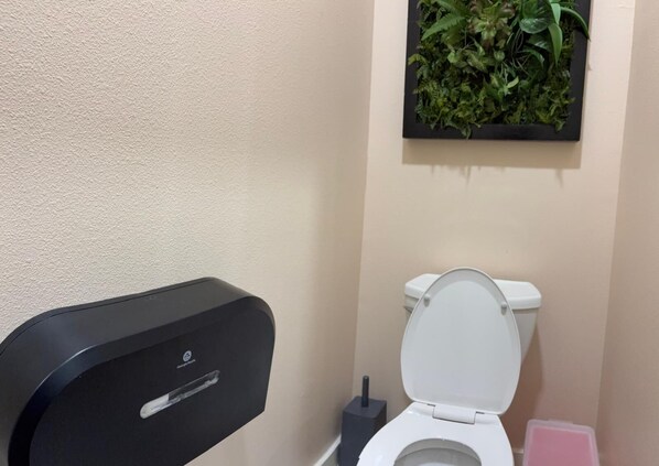 A bathroom with a toilet, a black trash bin, and a wall-mounted plant. - Charming 3-bedroom rooms with 2 full bath house with AC in Houston area! (Houston)