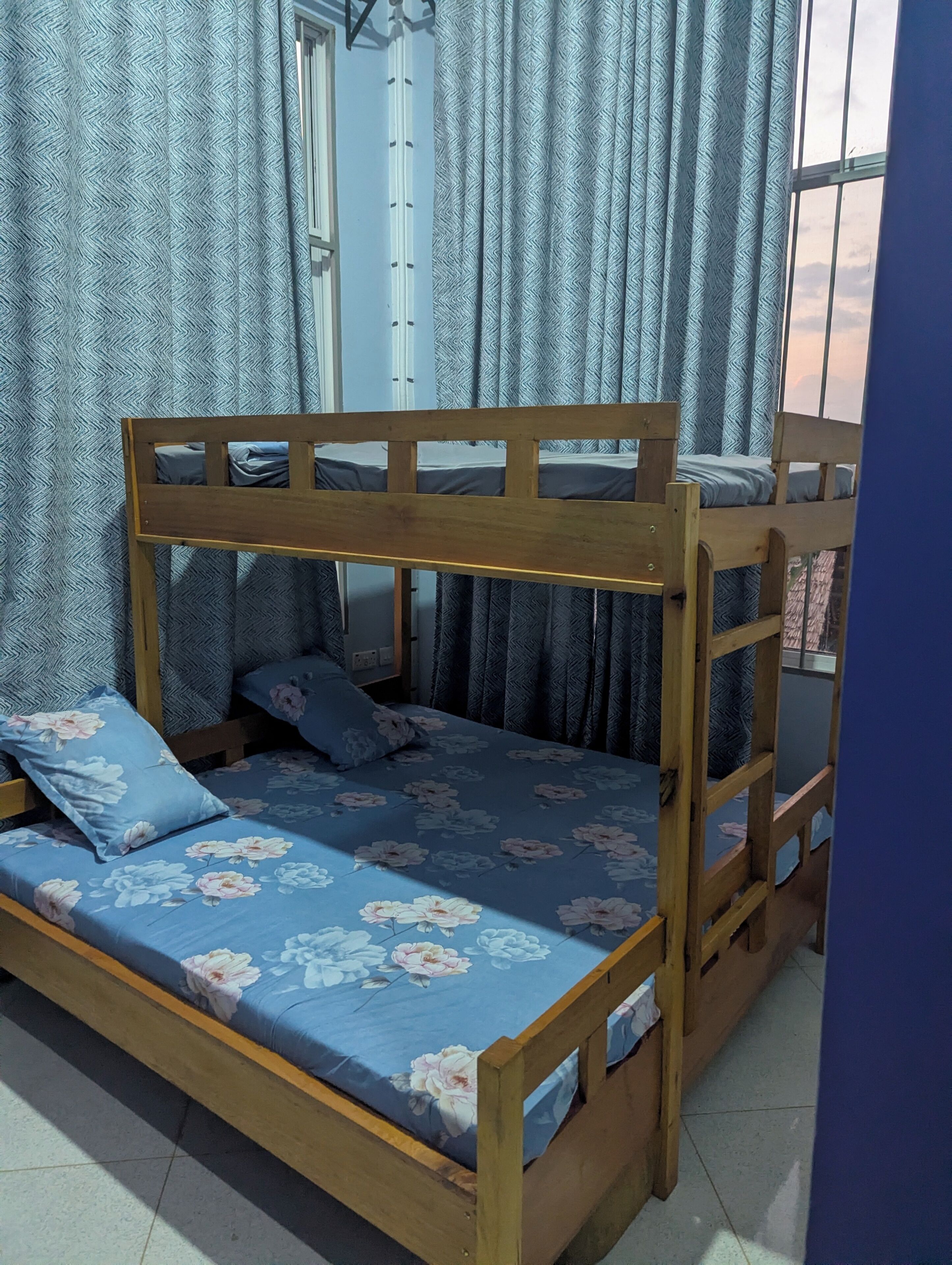 A bunk bed with floral bedding, a window with curtains, and a door in the background.