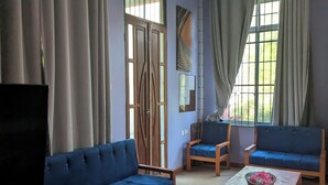 Ein Zimmer mit einem blauen Sofa, einem Holzstuhl, einem kleinen Tisch mit einer Schale und einem Fernseher.