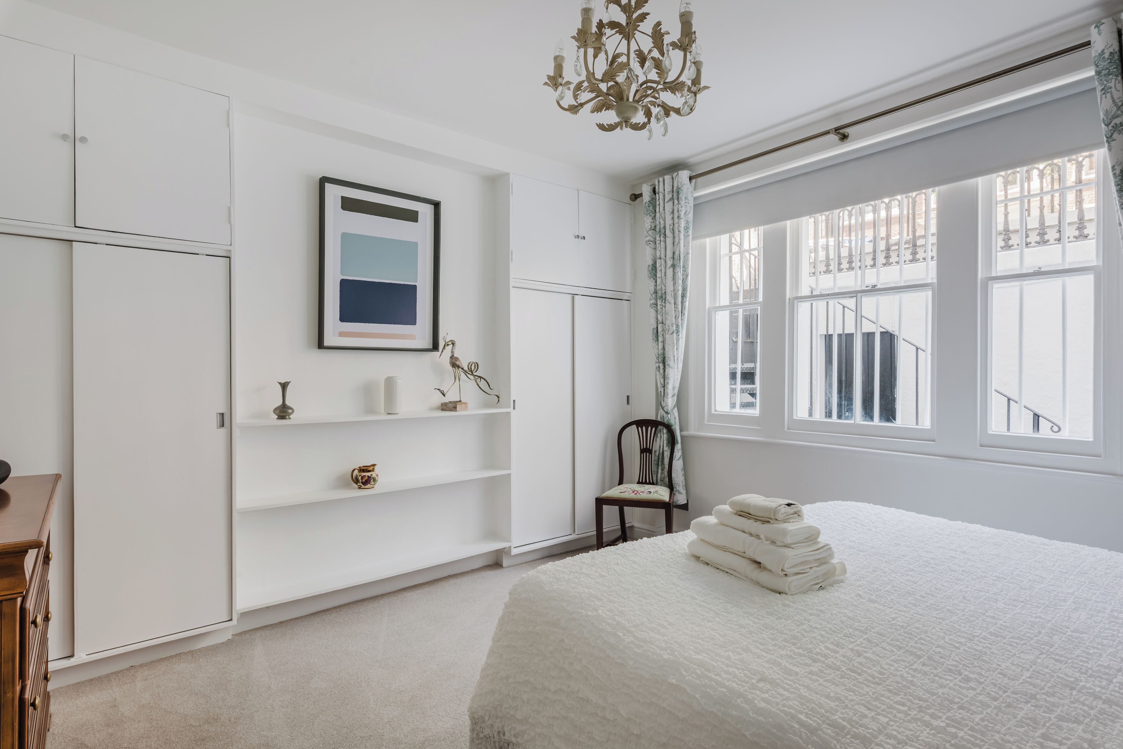 A bedroom with a large bed, a chandelier, a window with curtains, and a framed picture on the wall.