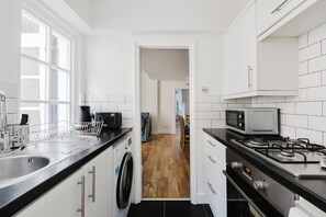 A modern kitchen with a dishwasher, microwave, and stove. - Chelsea Gem | Garden & Super King Bed (London)
