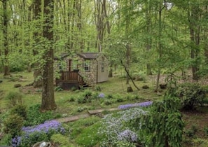 A rustic cabin surrounded by a dense forest with a wooden deck and stone walls. - Relax at Fairyland – Hot Tub, Pond, Gazebo & Woodland Escape (Birdsboro)