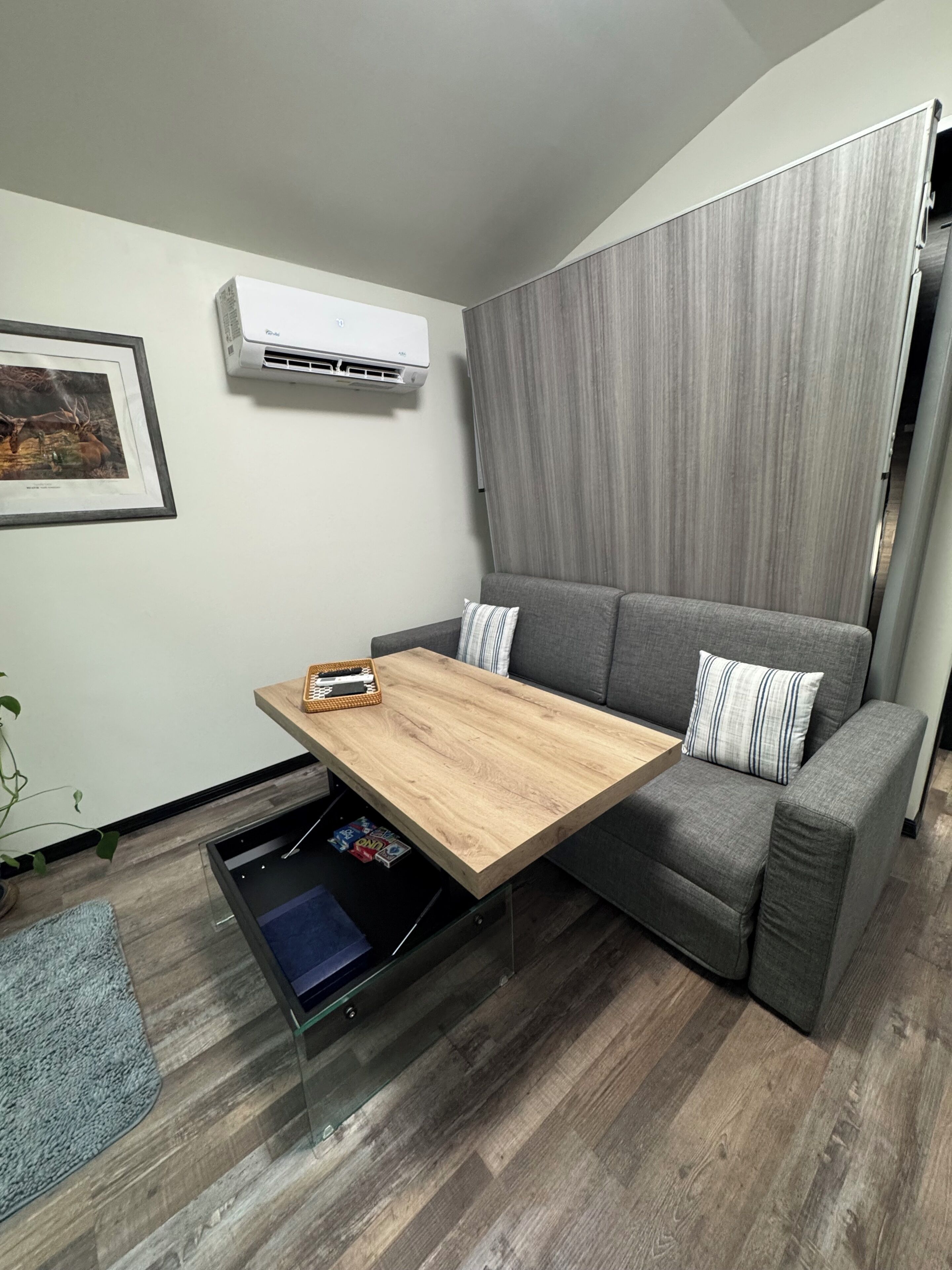 A modern living room with a gray sofa, a wooden coffee table, and a wall-mounted air conditioner.