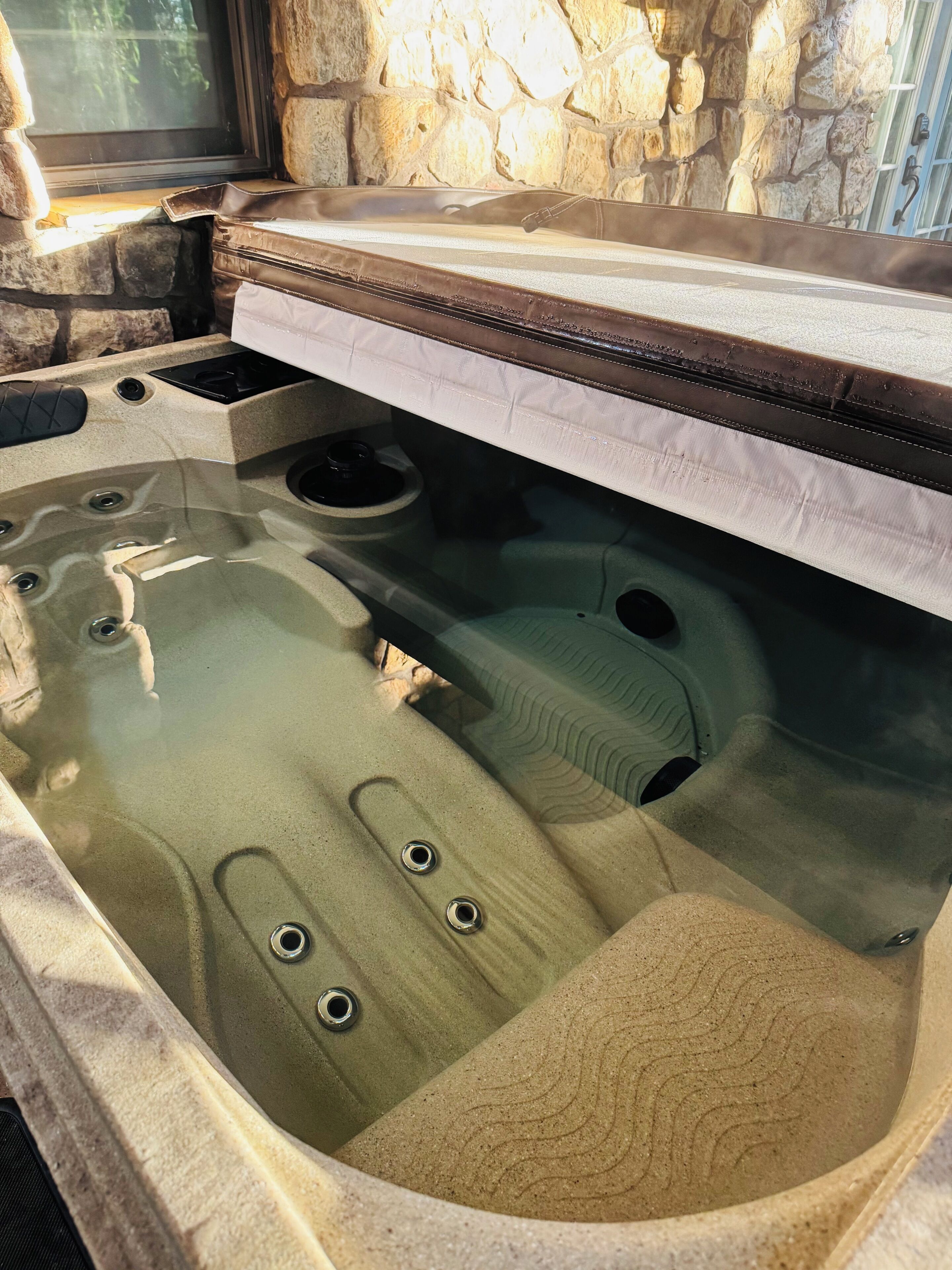 A hot tub with a stone wall backdrop, a window, and a stone countertop.