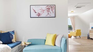 A modern living room with a blue sofa, a small table with a cup and book, and a framed artwork on the wall. - Waterfront - Sauna -steps To Beach! (Saco)