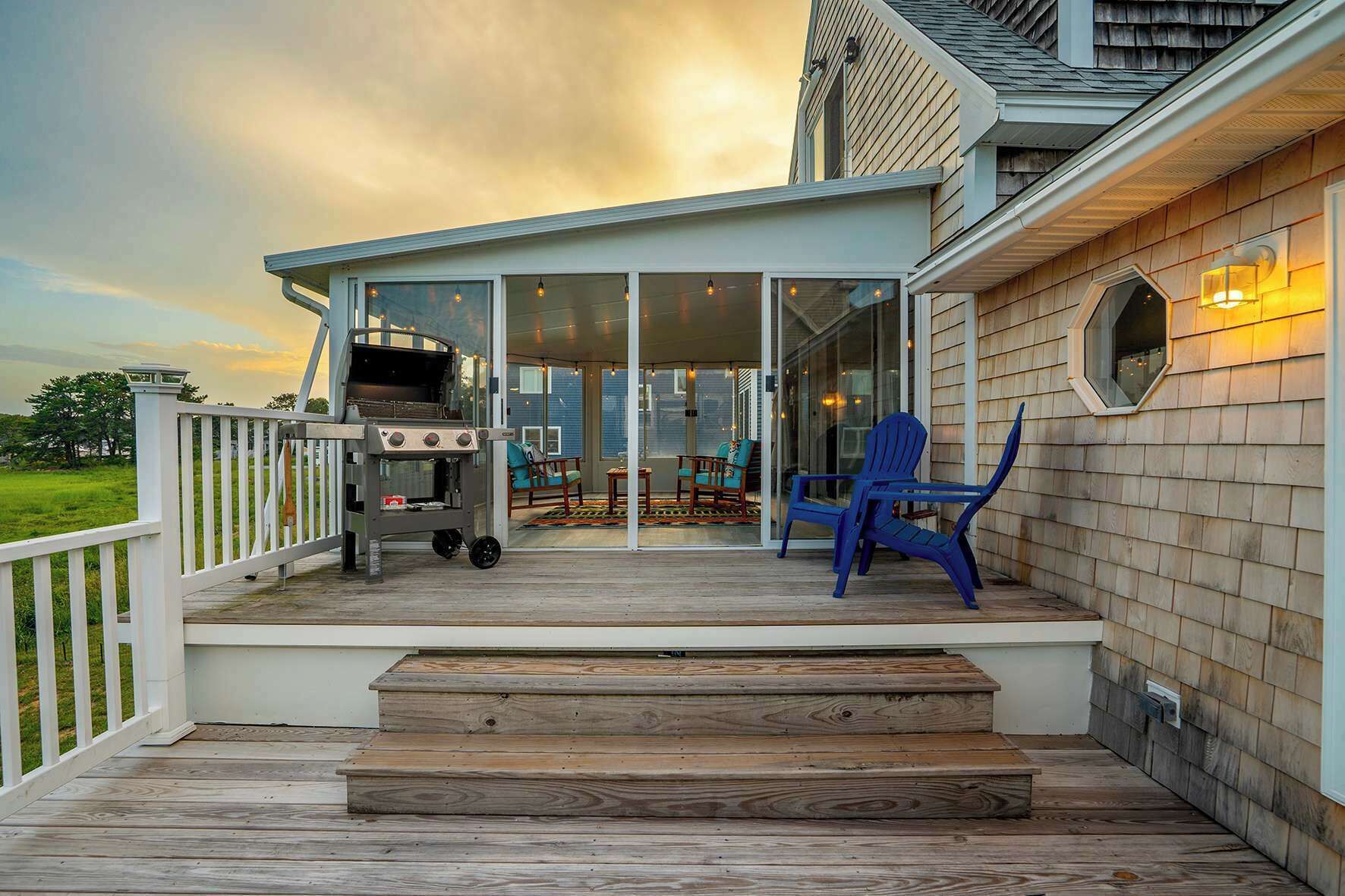 A covered deck with a grill, outdoor seating, and a view of the house.