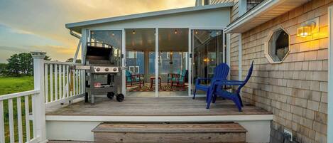 A covered deck with a grill, outdoor seating, and a view of the house.