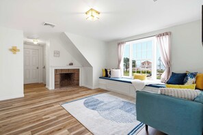 Una habitación con chimenea, ventana con cortinas, sofá con cojines y alfombra estampada.