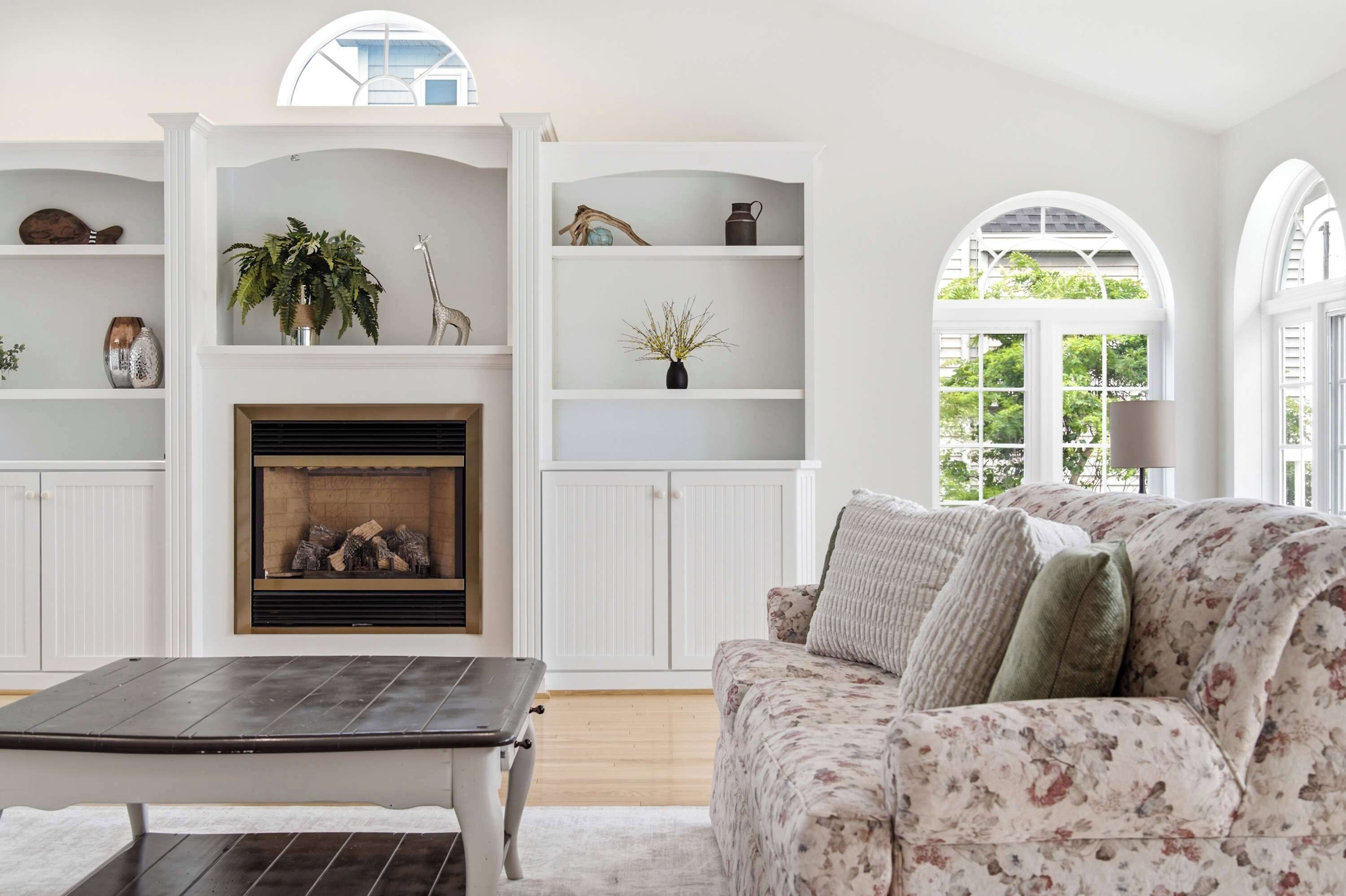A living room with a fireplace, white shelving, and a floral sofa.