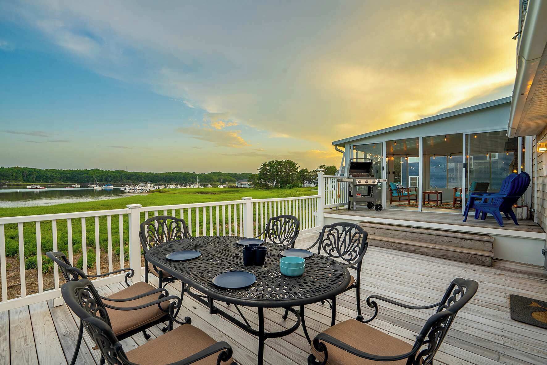 A deck with a table and chairs, overlooking a body of water and a grassy area.