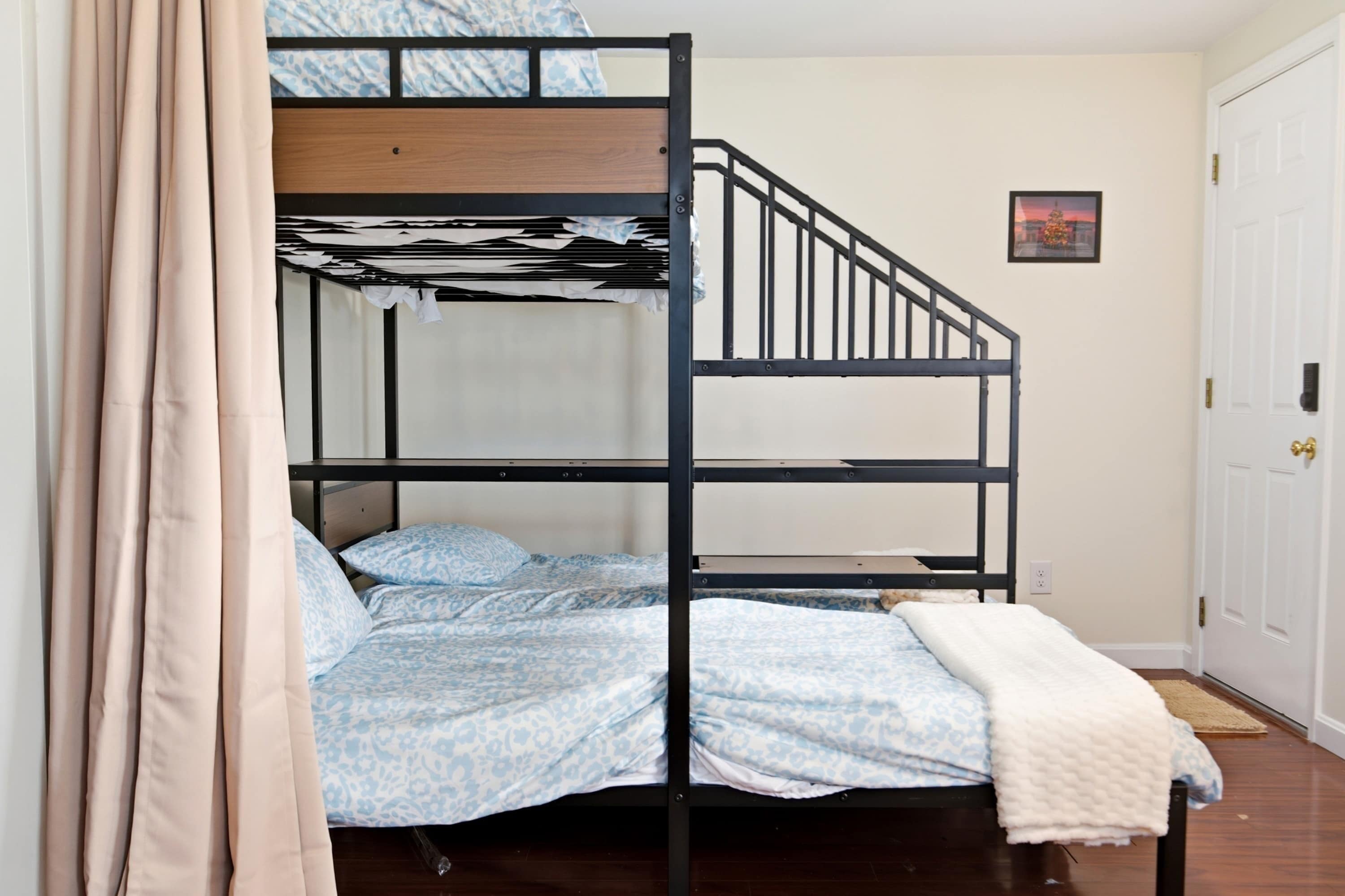 Une chambre avec un lit superposé doté d’une tête de lit en bois, un lit simple avec une literie à motifs et une porte blanche ornée d’un petit tableau au mur.